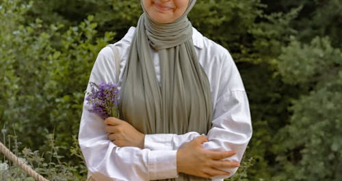 Smiling Woman with Crossed Arms Holding Bunch of Violet Flowers
