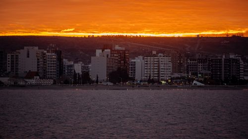 Free Vivid sunset illuminating city skyscrapers by the coastline with glowing orange sky. Stock Photo