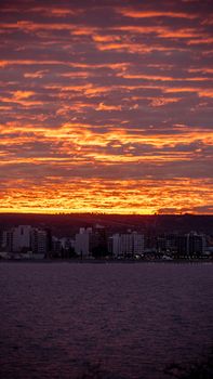 Dramatic sunset over a city skyline by the coast, showcasing vivid colors and silhouetted buildings.