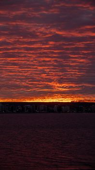 Stunning red sunset with cloud patterns over a coastal city skyline and sea.