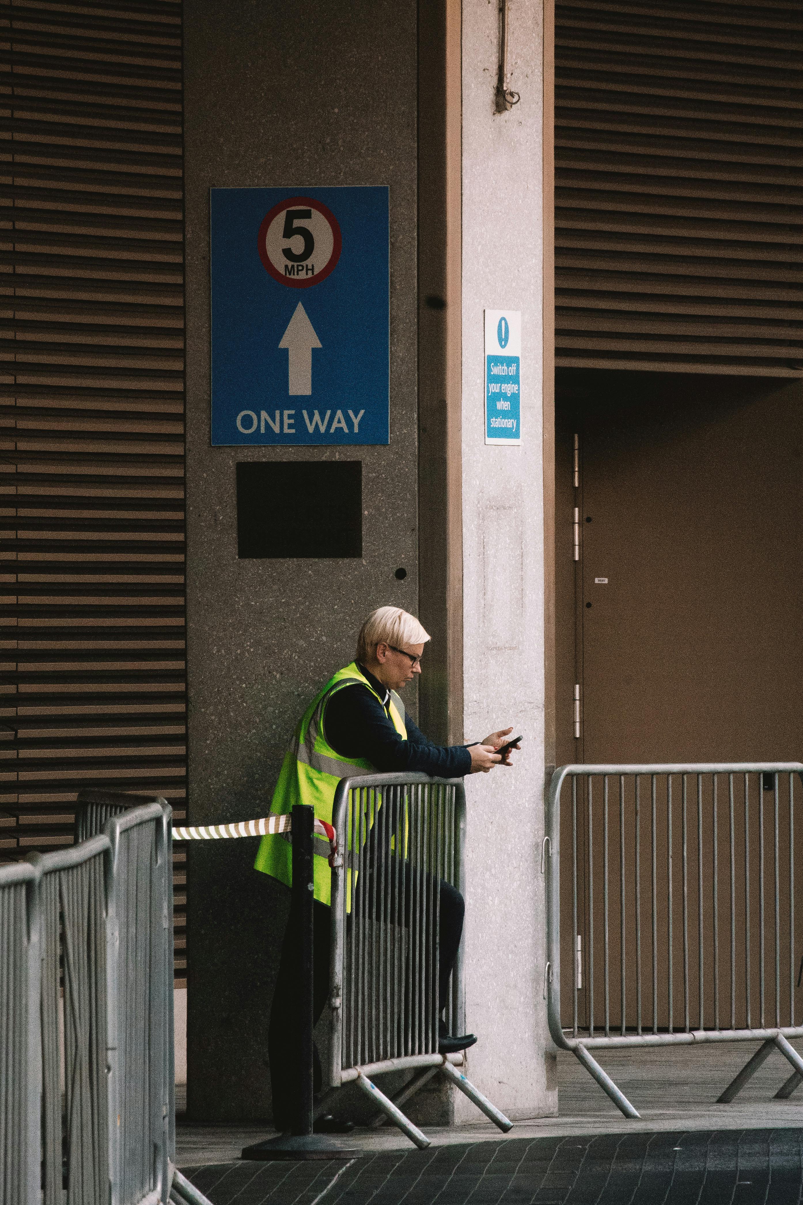 A safety officer stands by barriers in an urban London setting, ensuring security and traffic flow.