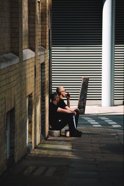 Free Two men sitting on a London street, capturing urban life in daylight. Stock Photo