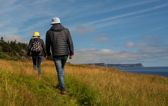 A couple hiking on a grassy coastal cliff with a scenic sea view under a clear sky.
