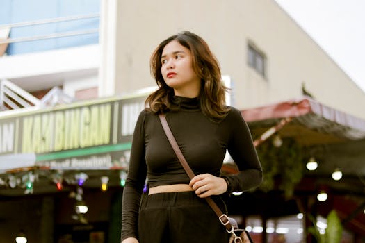 Stylish woman in black outfit confidently walking in an urban environment with a Kambingan restaurant backdrop.