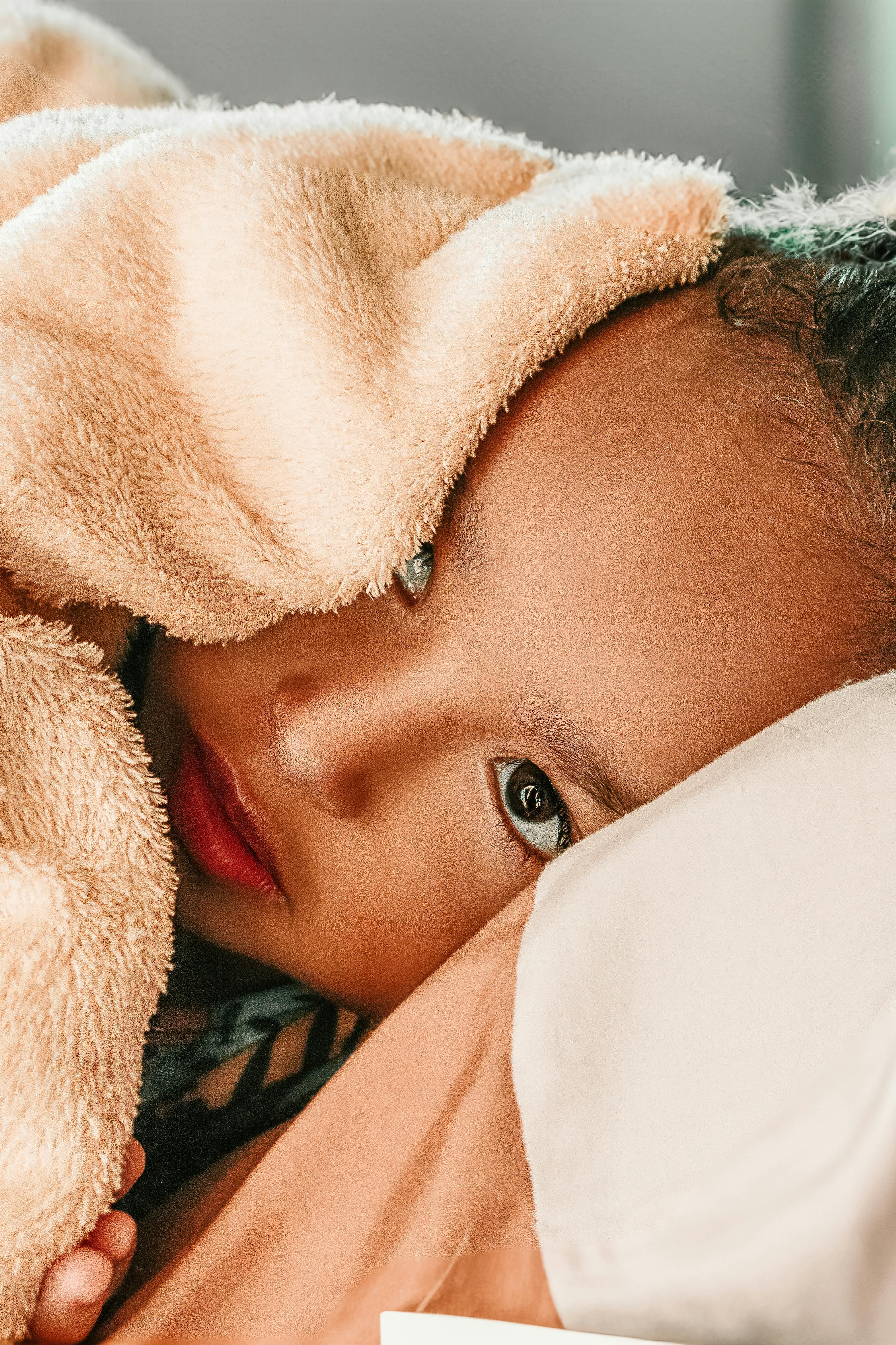A cute child peeks from under a soft, fluffy blanket indoors.