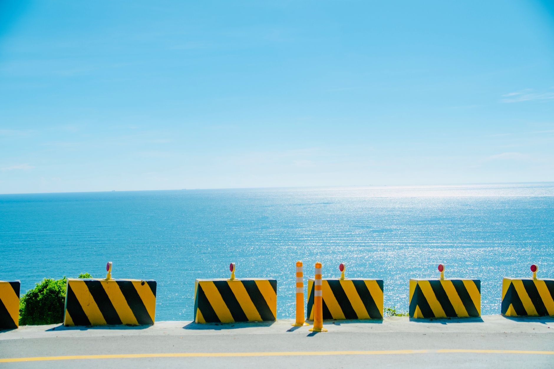 A vibrant view of road barriers against a shimmering seascape under a bright blue sky.