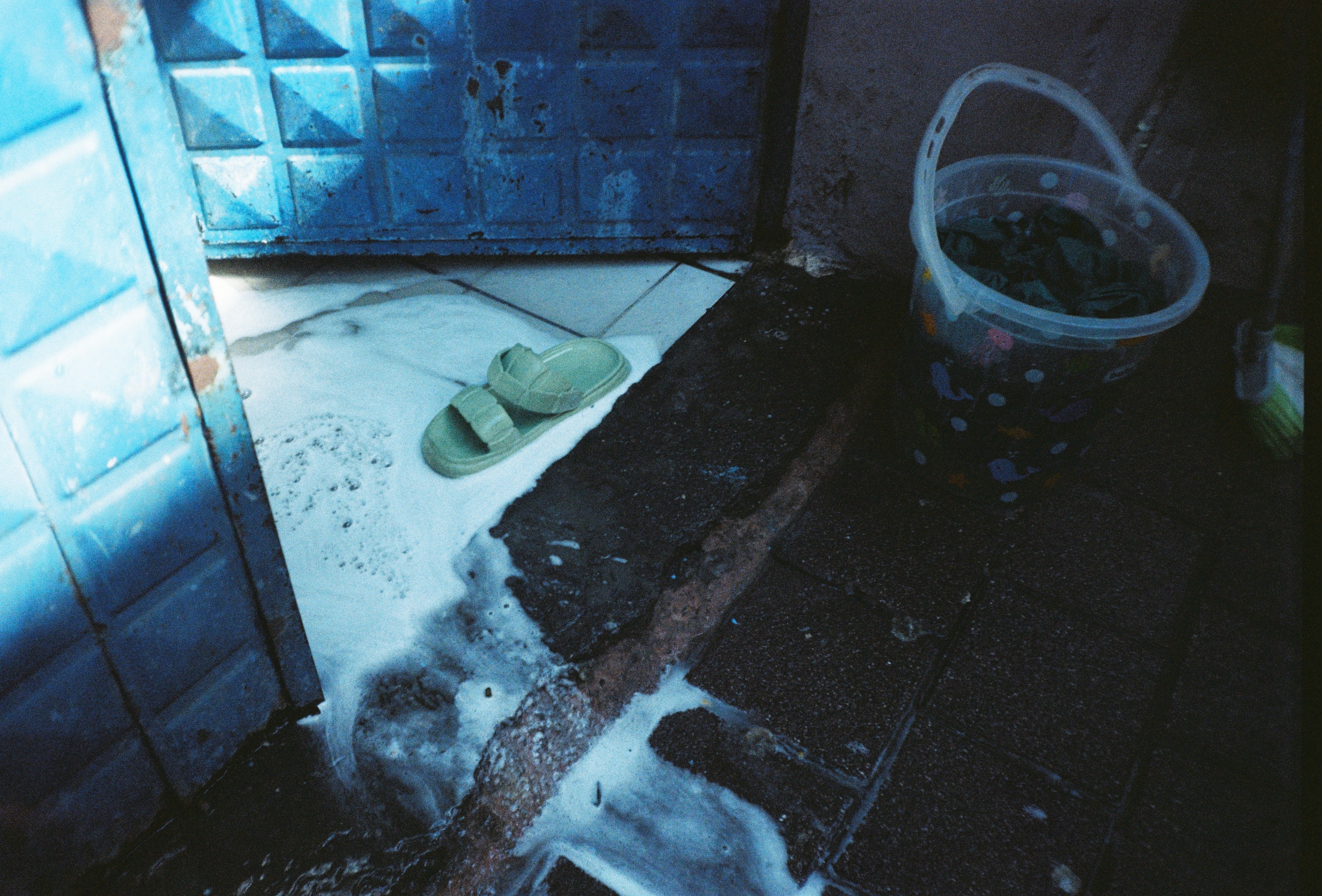 Flooded entrance with a bucket and slippers in standing water