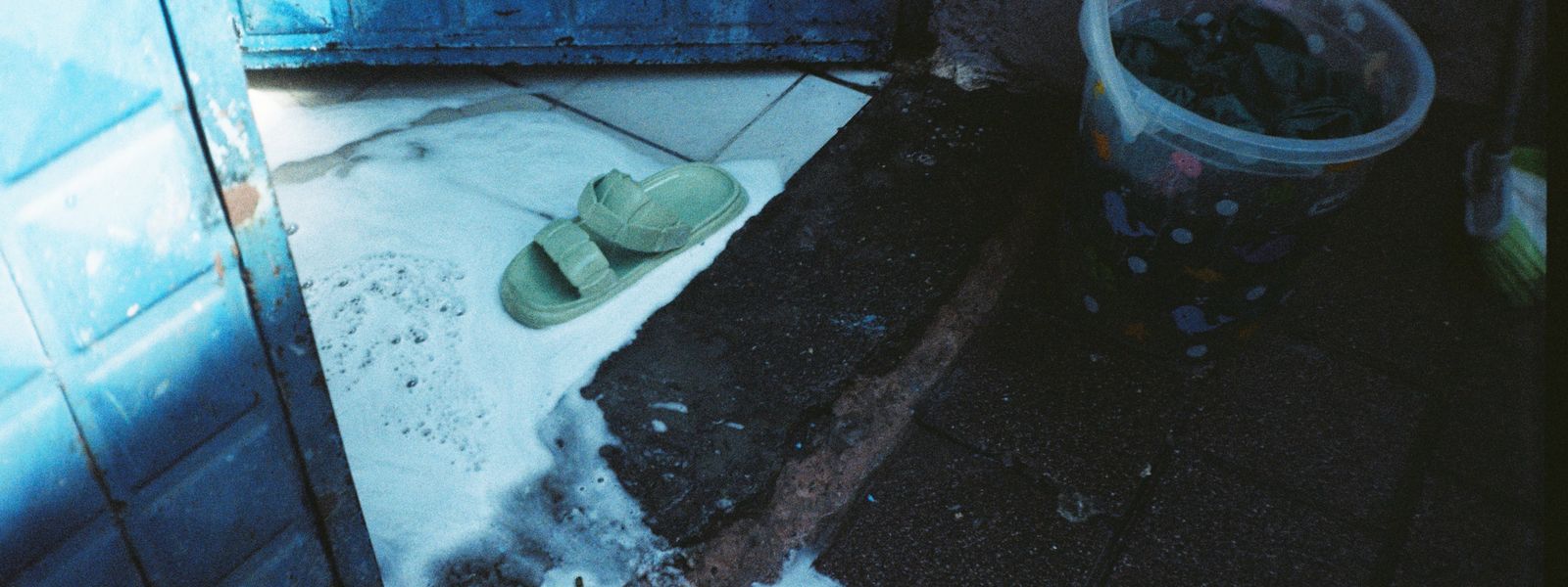 Flooded entrance with a bucket and slippers in standing water