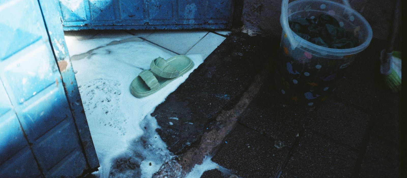 Flooded entrance with a bucket and slippers in standing water