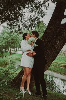 Bride and groom sharing a loving kiss by a tree in a park, celebrating their wedding day.