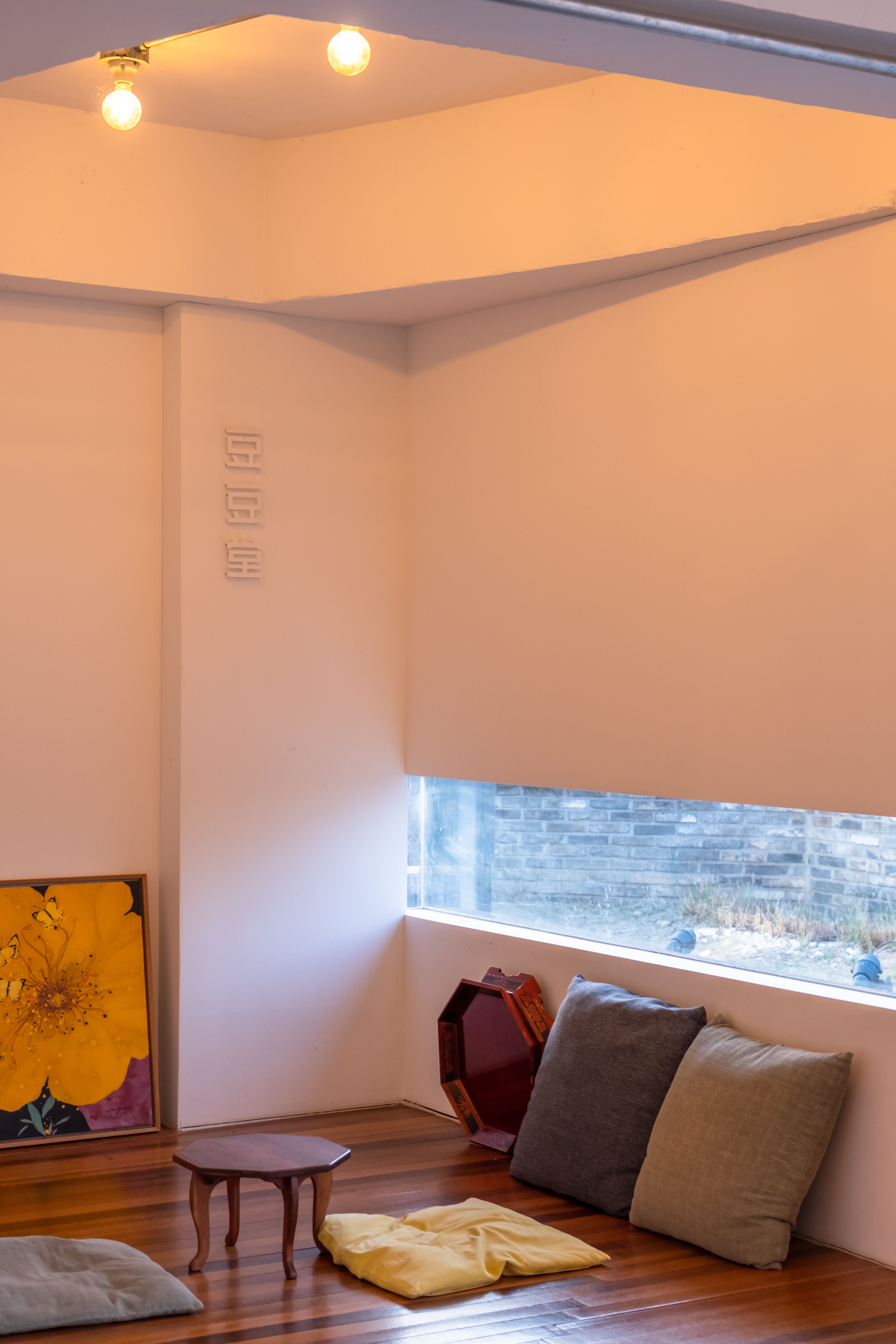 A minimalist room setup featuring cushions, low table, and art near a window.