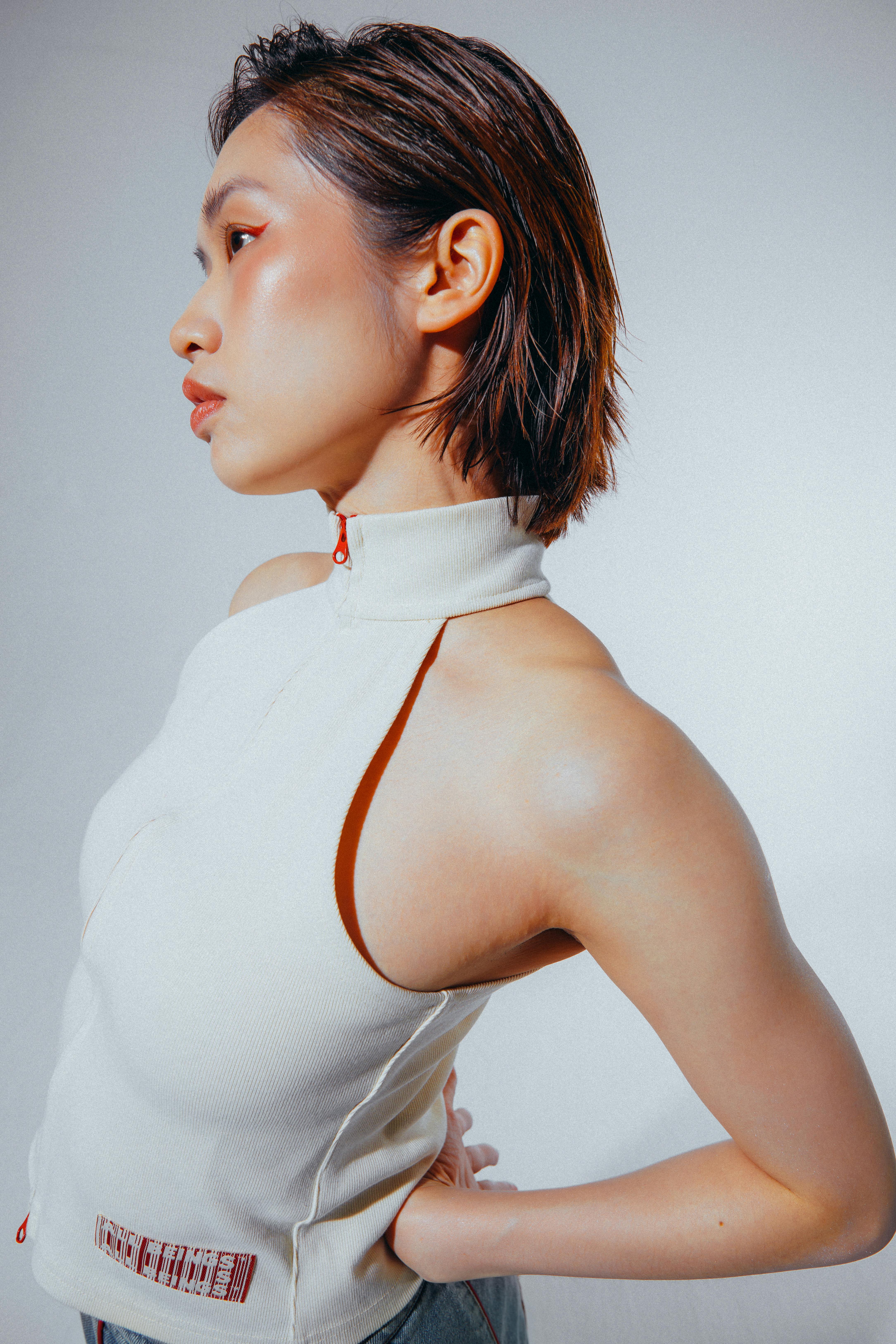 Free Side profile of a stylish woman in a white halter top against a plain background. Stock Photo