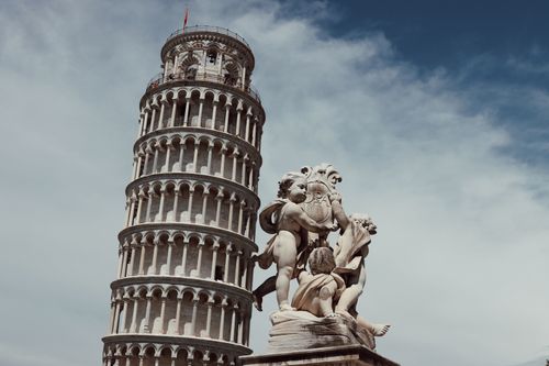Free View of the Leaning Tower of Pisa with a nearby classical statue under a clear sky. Stock Photo