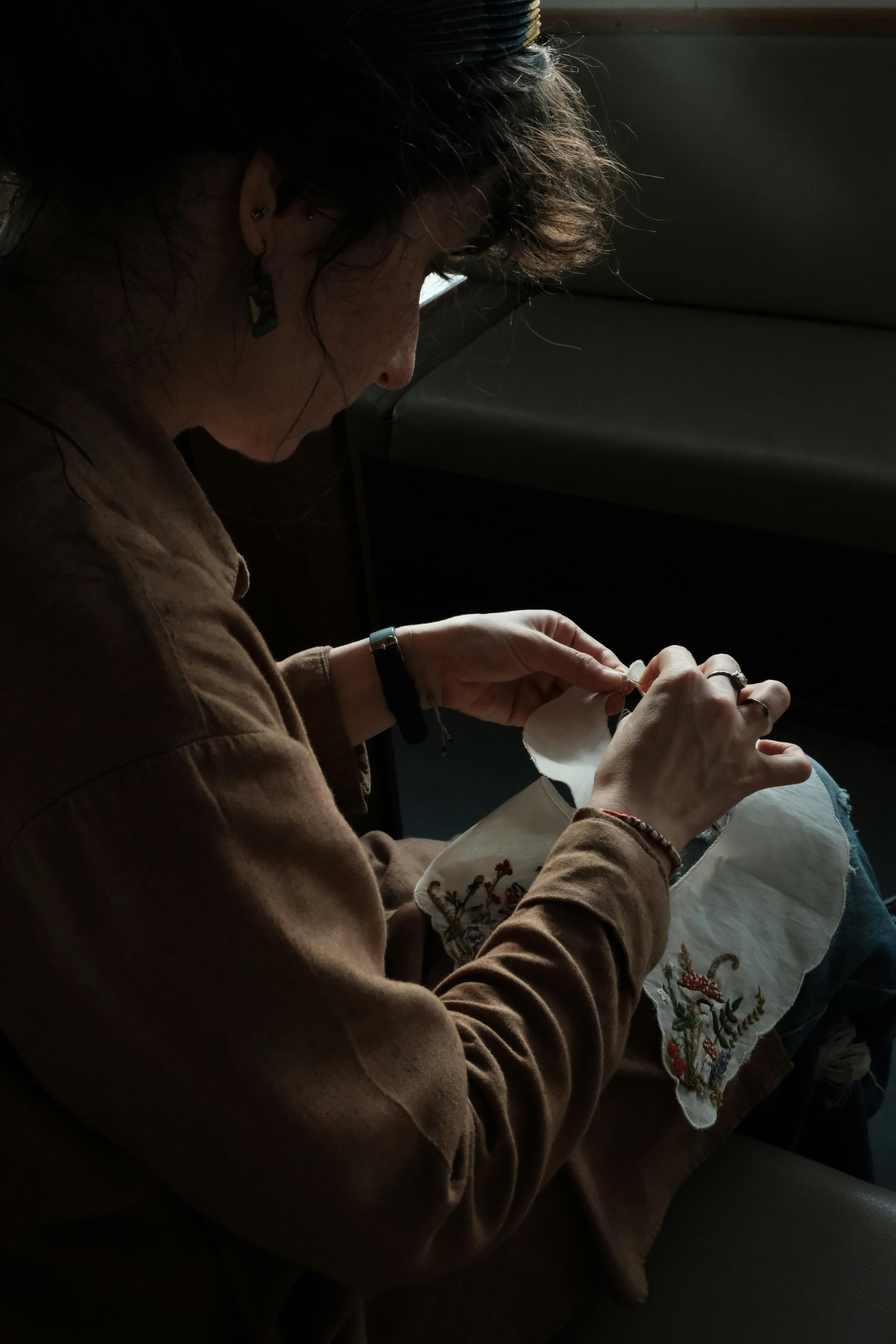 Focused woman embroidering with intricate design. Captured in a dim setting for dramatic effect.