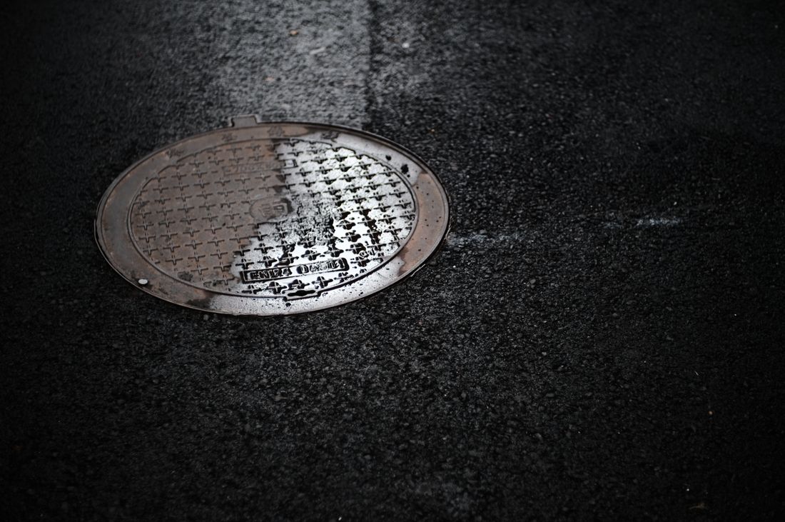 Plaque d'égout sur une rue mouillée, reflets de pluie.