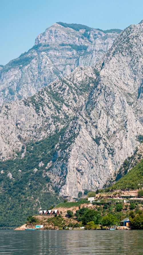 Free Breathtaking view of rugged mountains towering over a serene lake with small huts dotting the shoreline. Stock Photo