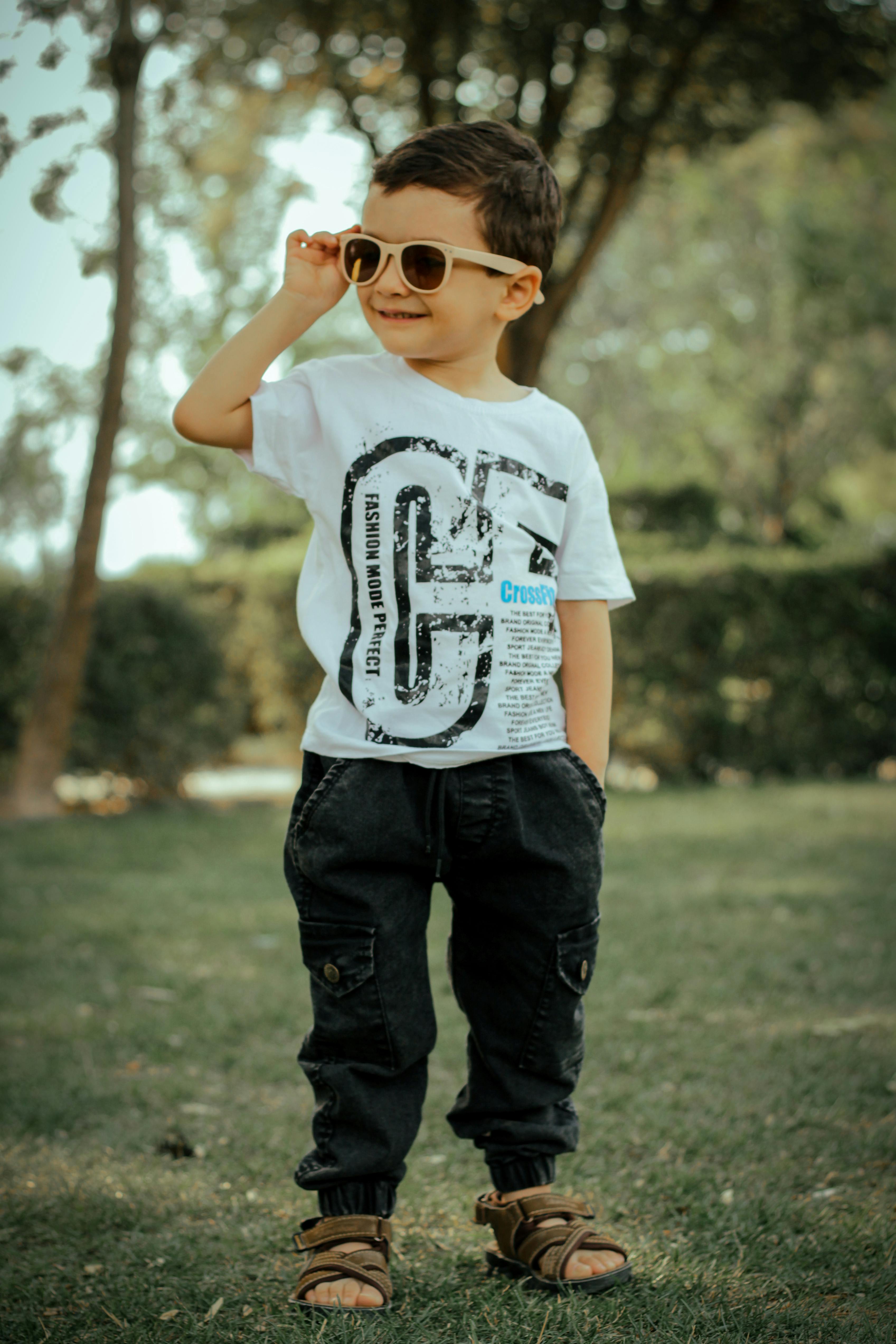 Free A fashionable young boy in sunglasses and casual wear enjoying a sunny day at the park. Stock Photo