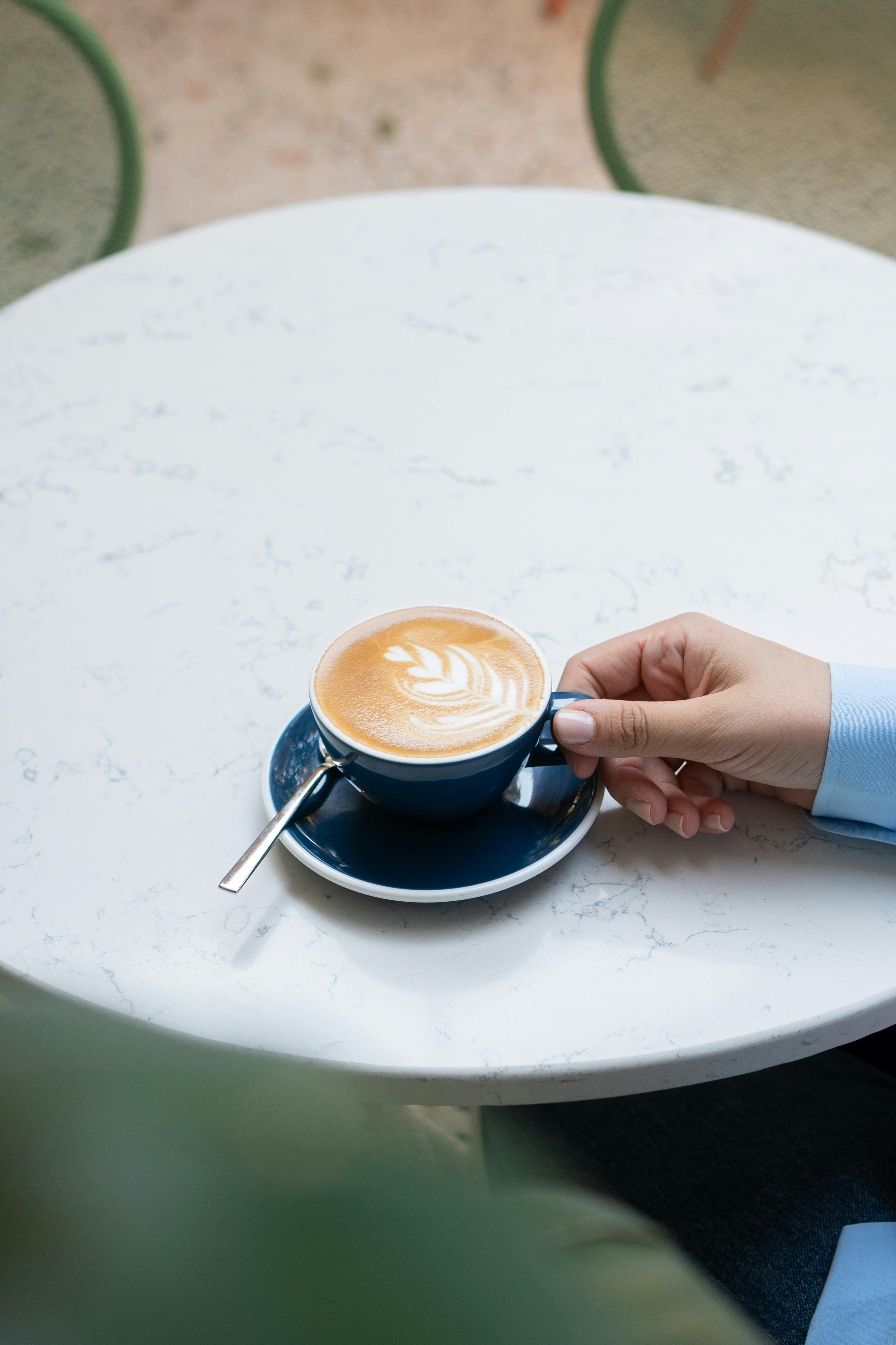 A person holding a latte in a blue cup on a marble table, perfect for coffee lovers.
