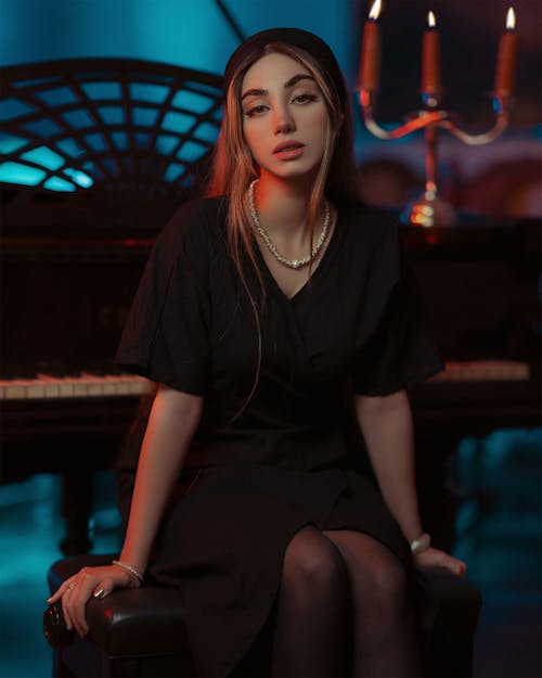Gorgeous Woman with Necklace in Black Dress Sitting by Piano