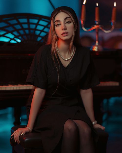 Free A fashionable woman in a black dress sits by a piano, exuding elegance and charm. Stock Photo