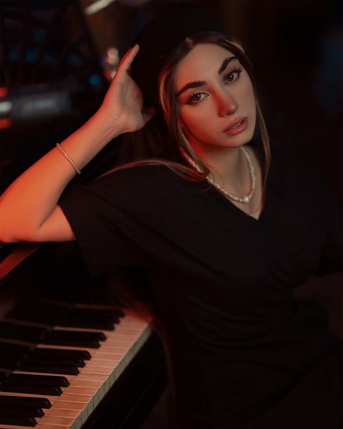 Free Stylish woman in black dress posing with a piano in dramatic lighting. Stock Photo