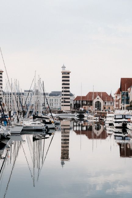 Harbor view with sailboats and lighthouse reflection in Deauville, France.