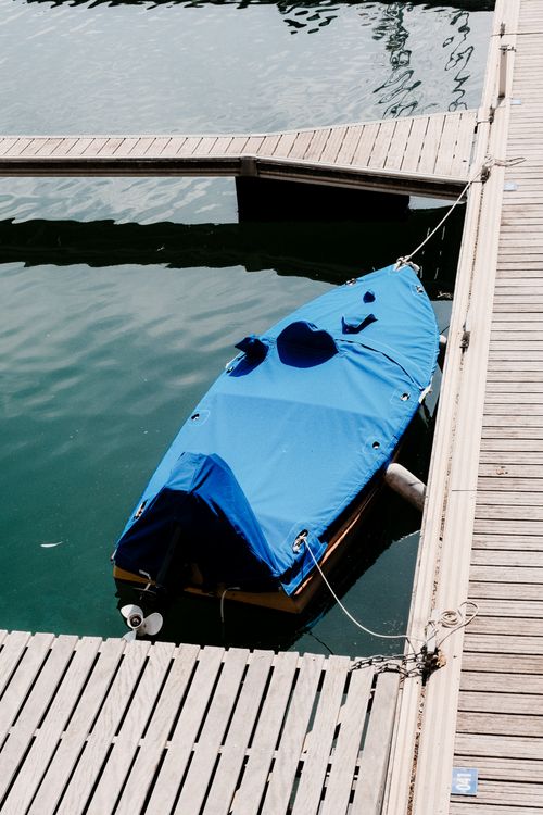 Free Aerial view of a small blue-covered boat moored at a wooden dock on calm waters. Stock Photo