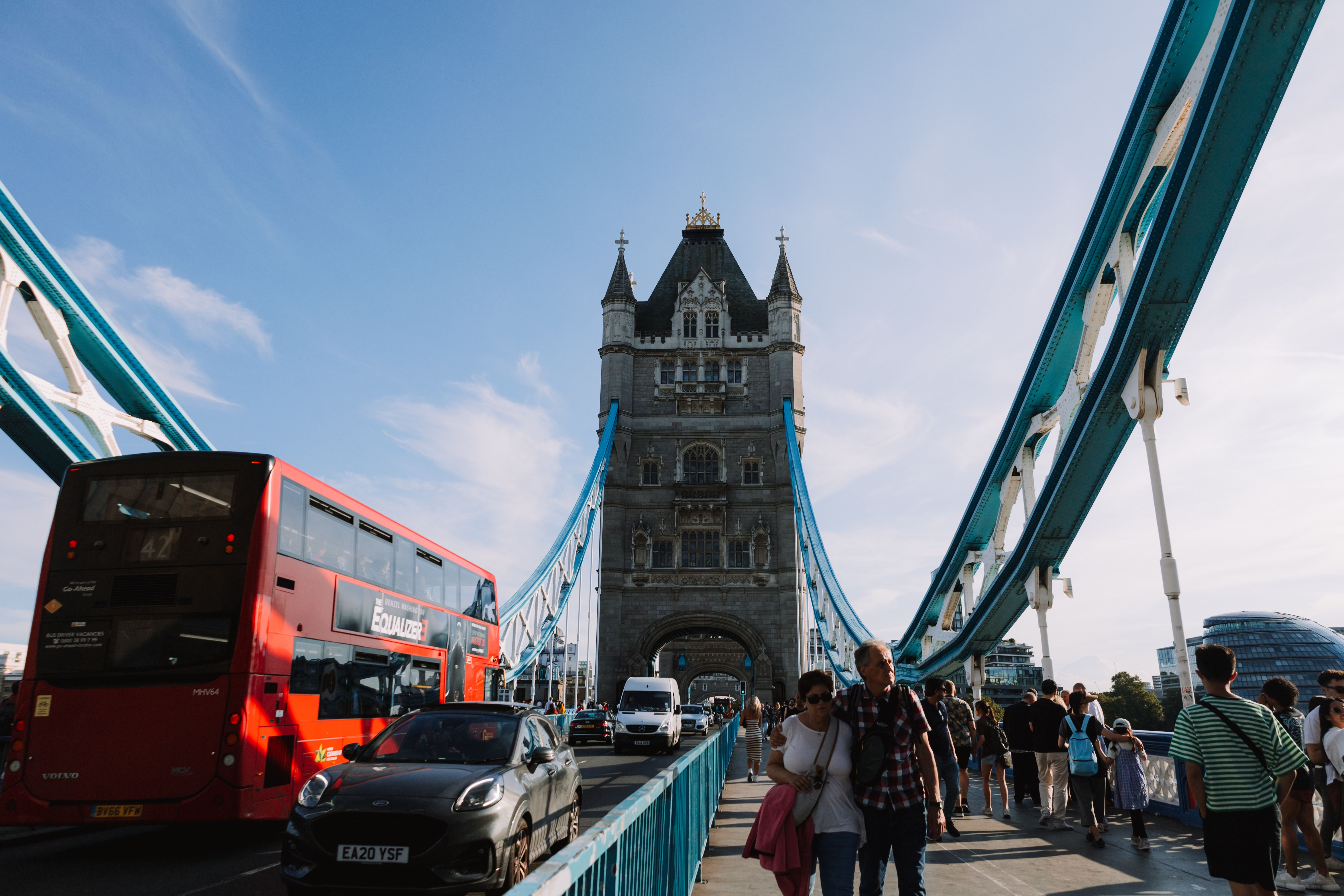 Dynamic street life on Tower Bridge in London with buses, cars, and people under a clear sky.