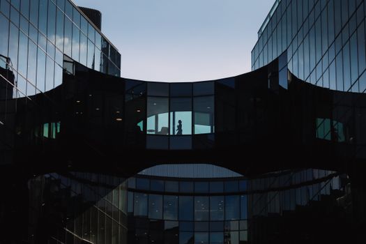 A striking view of contemporary glass buildings in London with silhouetted figures on a skybridge.