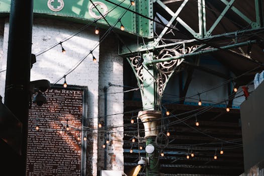 Intricate ironwork beams and string lights create a vintage urban atmosphere in London's historic district.