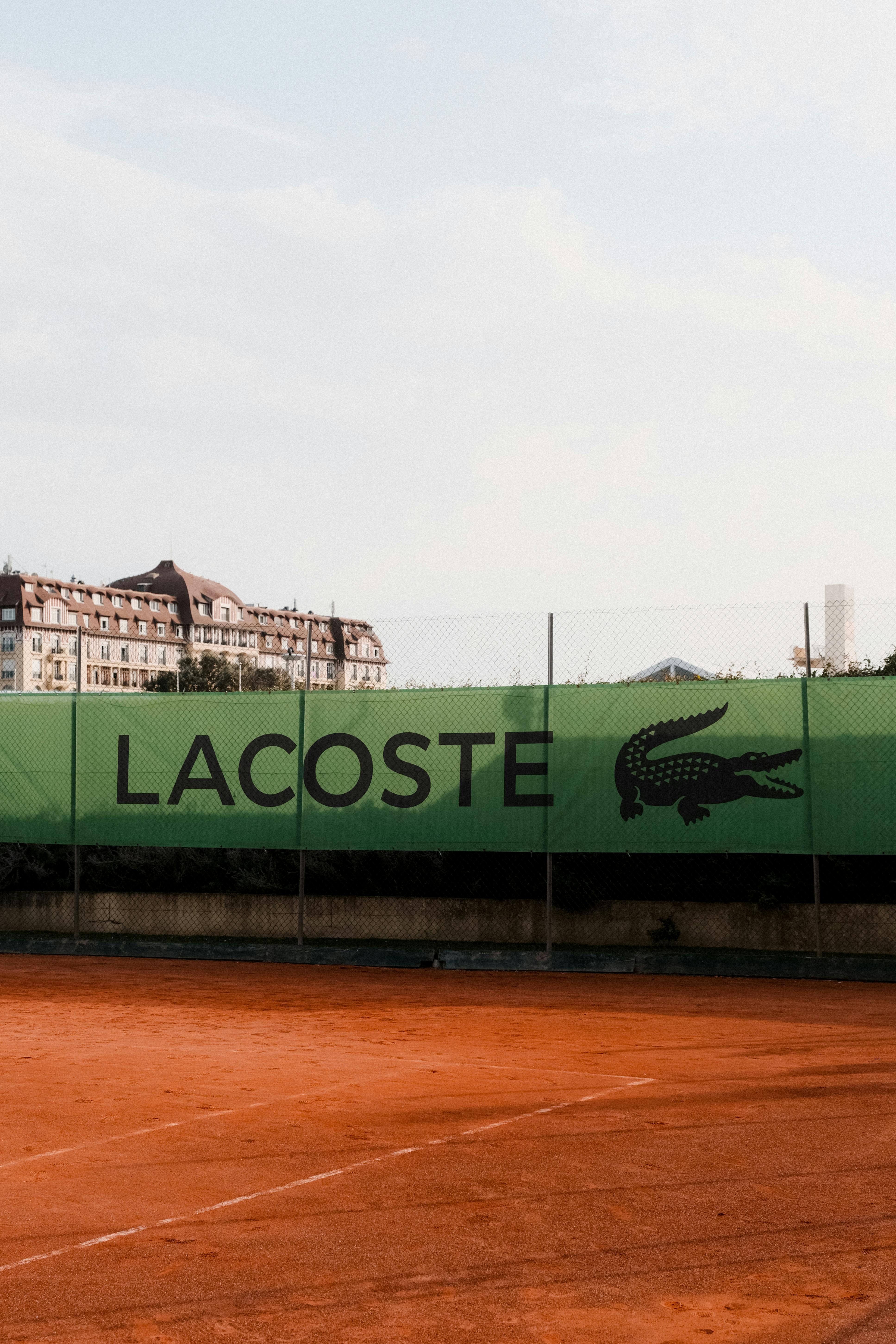 Lacoste branded banner on an outdoor tennis court under a clear sky, showcasing sports advertising.