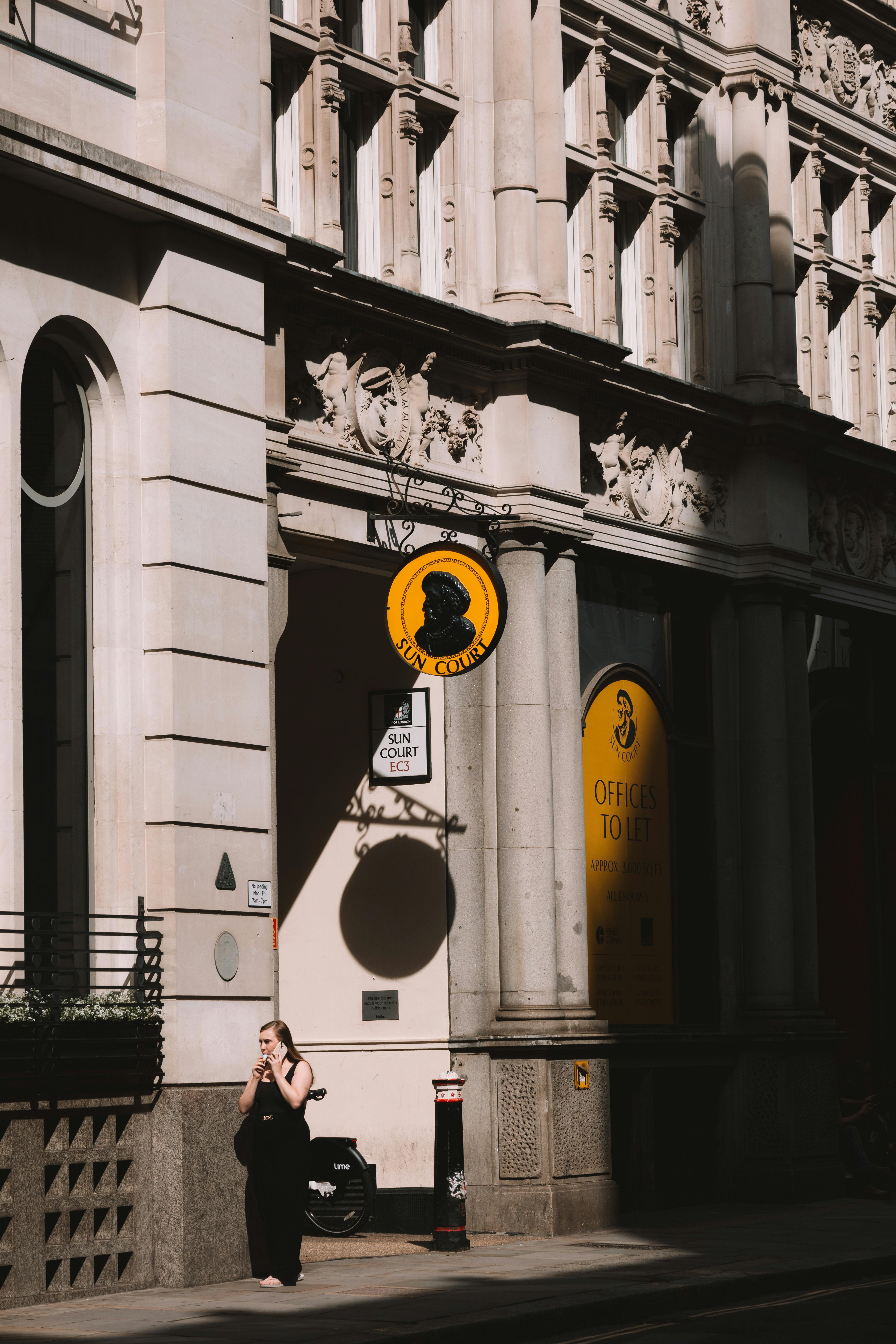 A woman walks past an ornate building in sunlit London, capturing urban architecture.