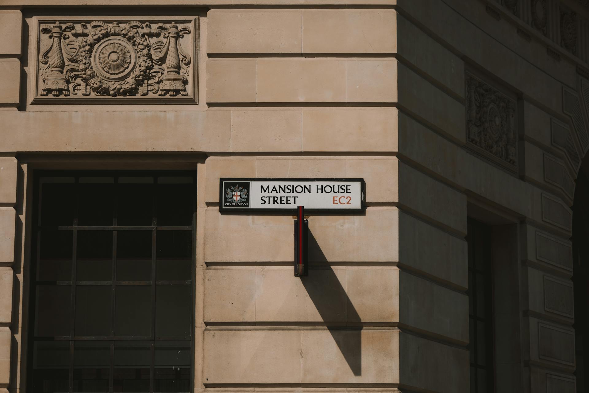 Sunlit view of Mansion House Street sign on a historic wall in London, England.