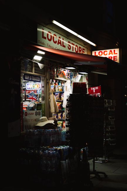 Brightly lit local store front at night, showcasing a variety of goods.