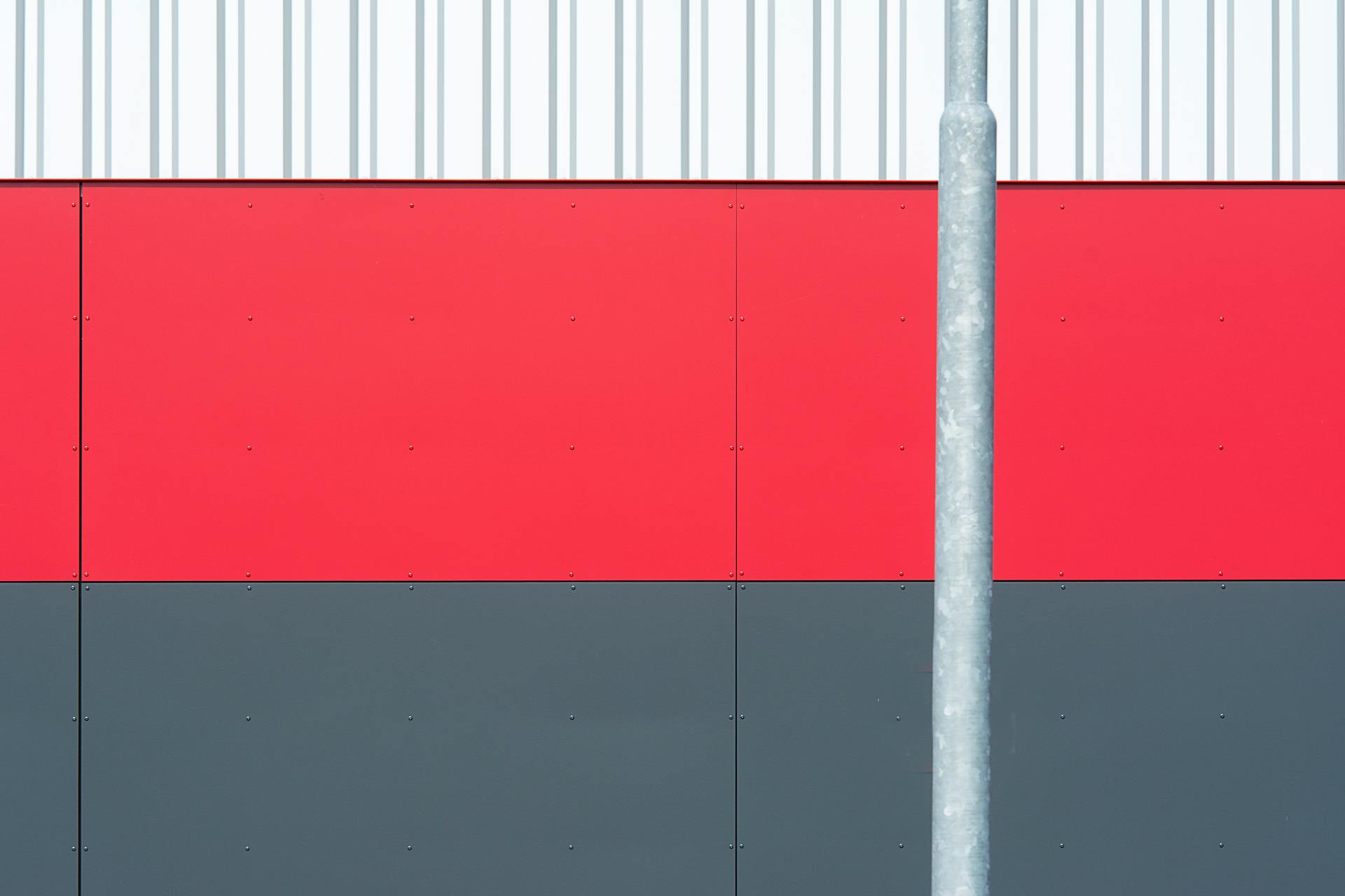 A minimalist industrial wall with red, gray panels and corrugated metal in vivid geometric pattern.