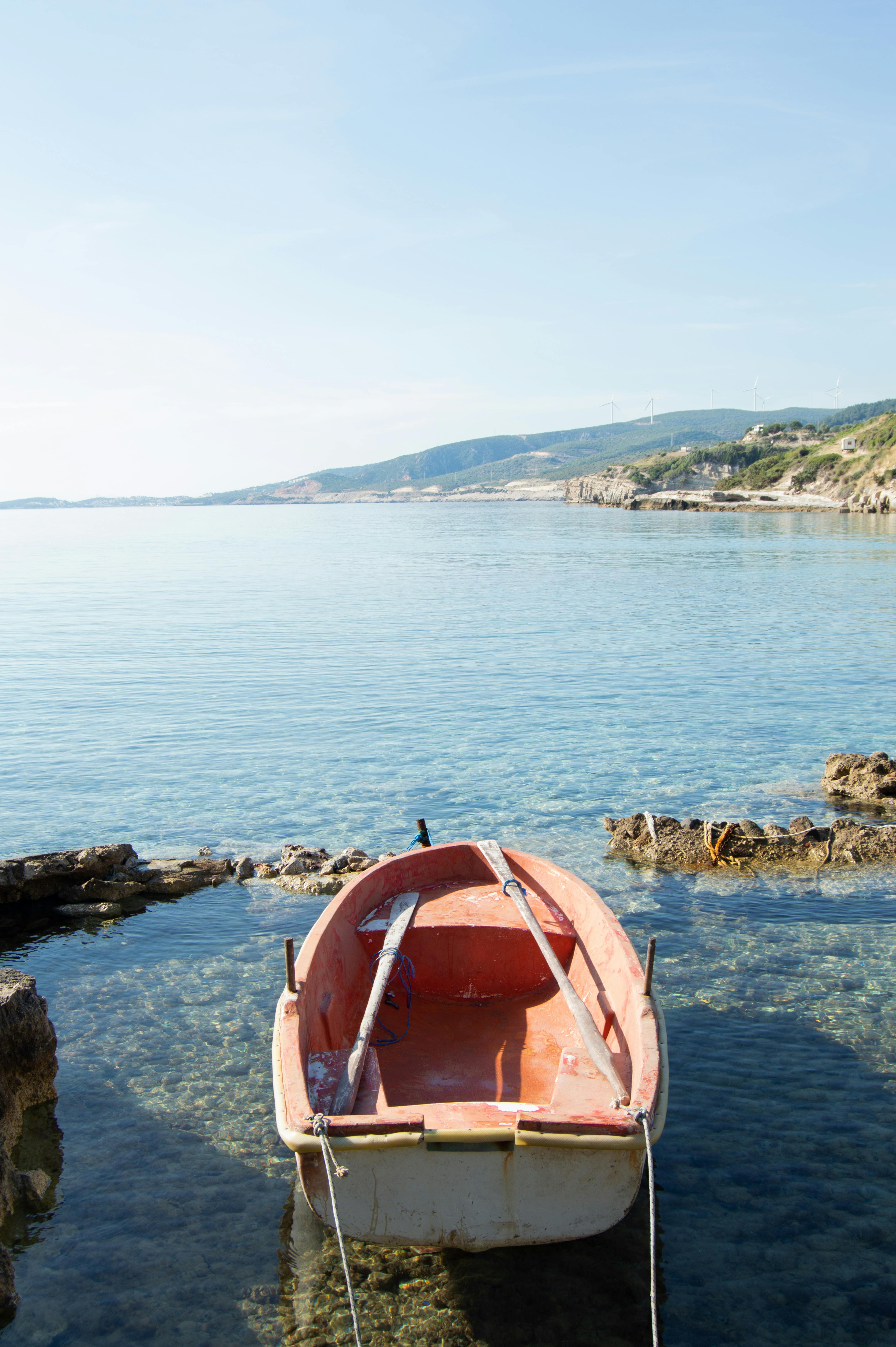 A serene view of a rowboat on the clear waters of Karaburun, İzmir, with rocky shores and distant hills.