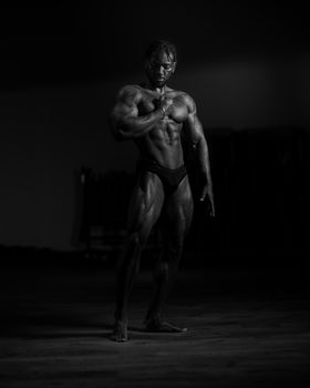 Black and white photo of a muscular man posing in a studio, showcasing bodybuilding aesthetics.