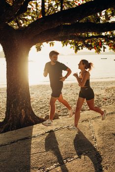 A man and woman jogging under a tree on Niterói beach at sunrise, embracing fitness and nature.