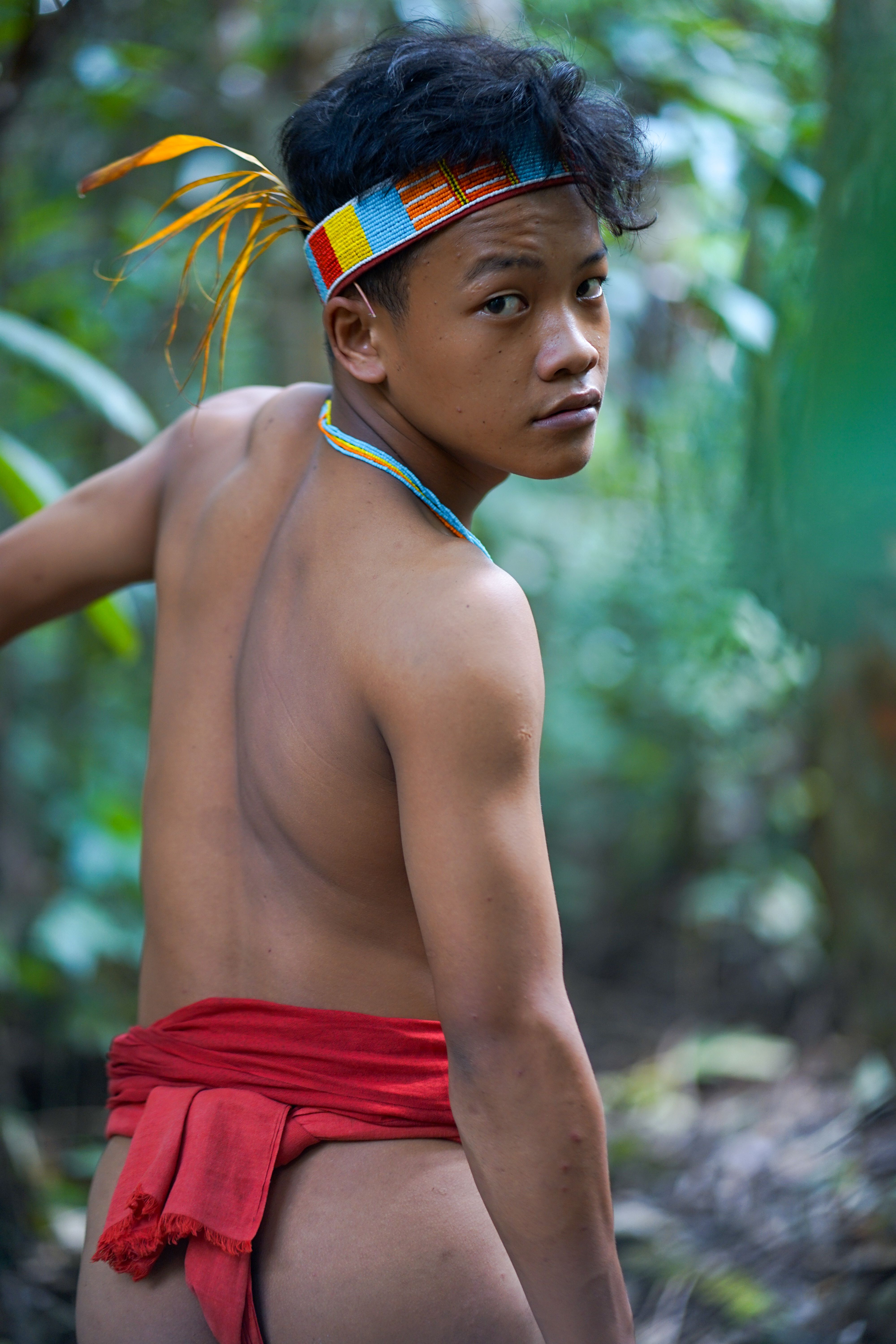 A teenager in traditional tribal attire stands in the lush jungle of West Sumatra, Indonesia.