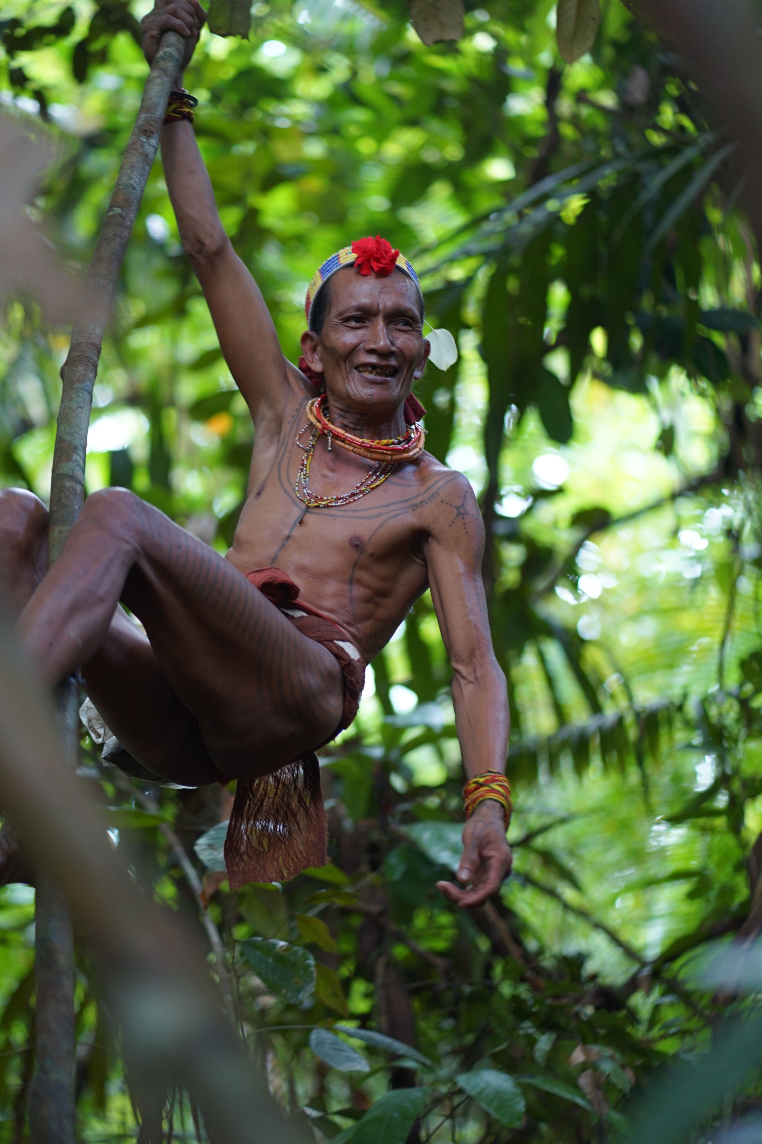 Man in tribal attire smiling while climbing tree in dense jungle.