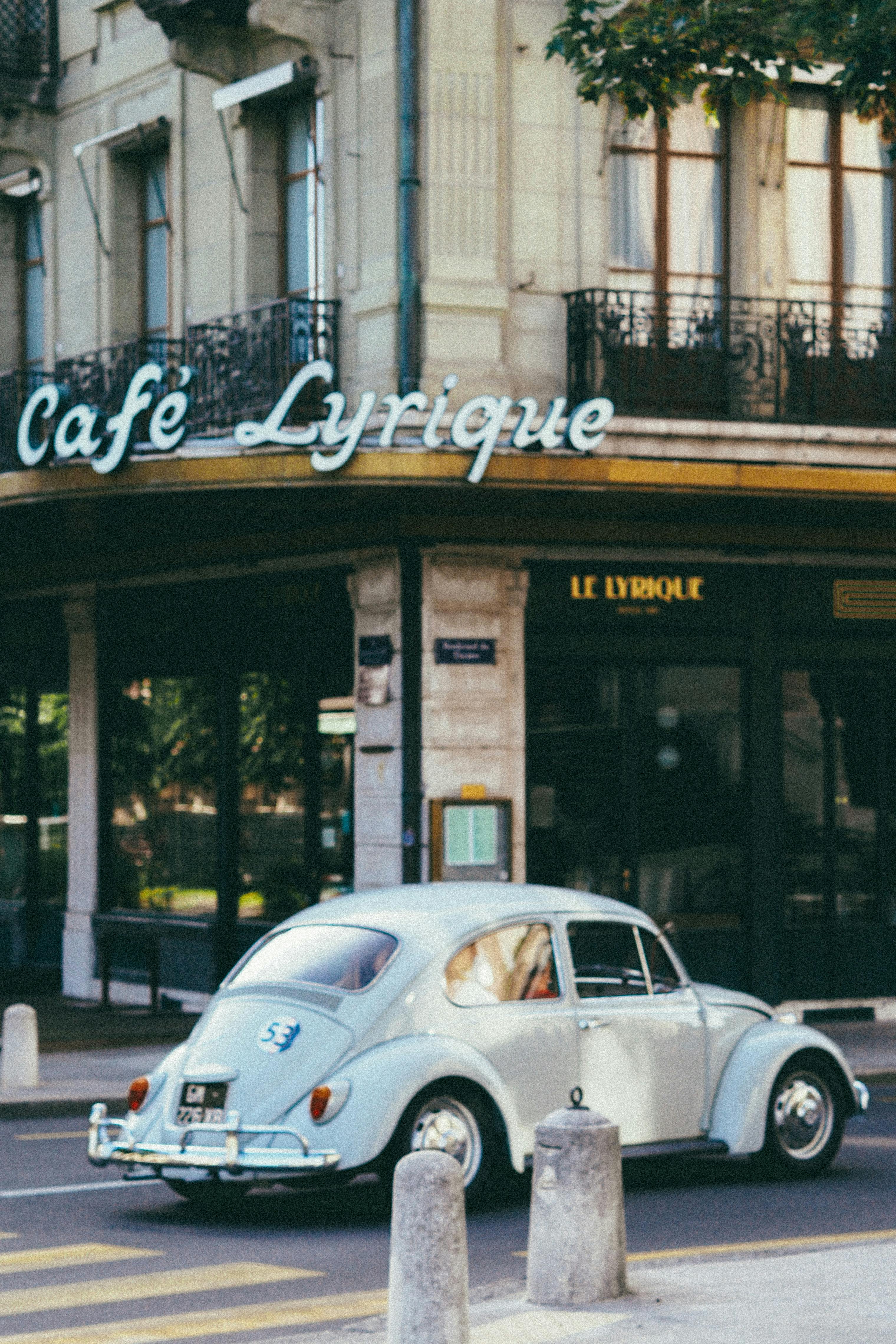 Classic Volkswagen Beetle parked near Café Lyrique in a European city street.