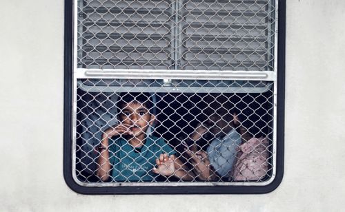 Free A child gazes through a metal mesh train window reflecting life's journey. Stock Photo