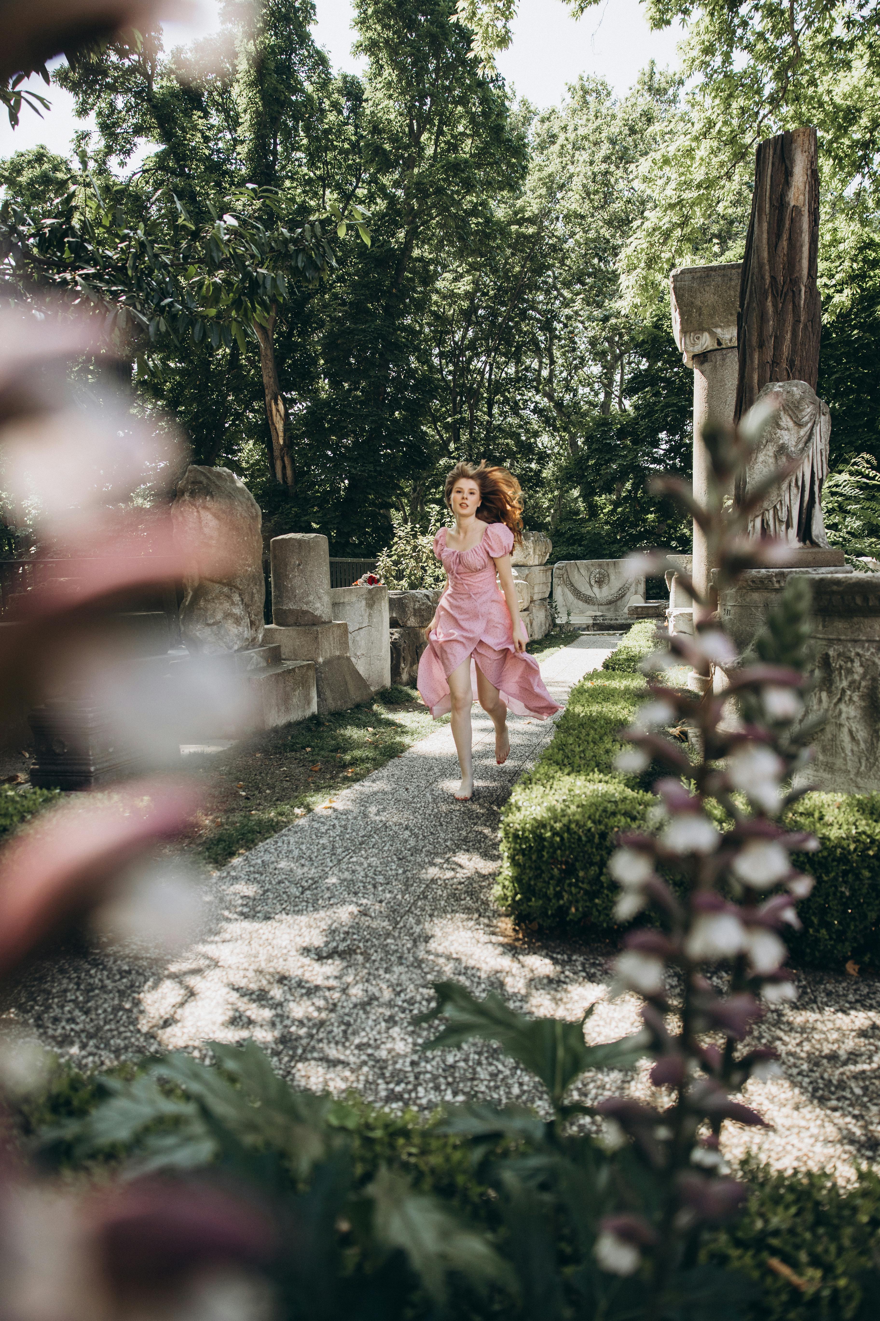 a woman in a pink dress walking through a garden