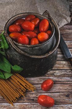 A rustic display of fresh cherry tomatoes with spaghetti and basil on a wooden surface.