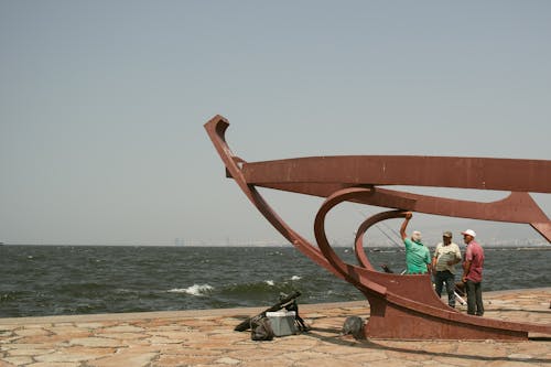 Elderly Men Standing by Sculpture on Sea Shore