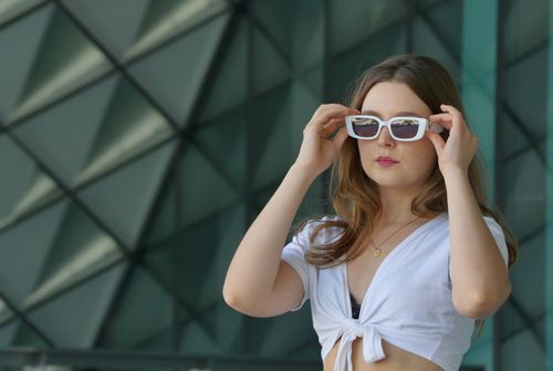 Free A fashionable woman wearing sunglasses posing confidently in a sunlit urban setting. Stock Photo