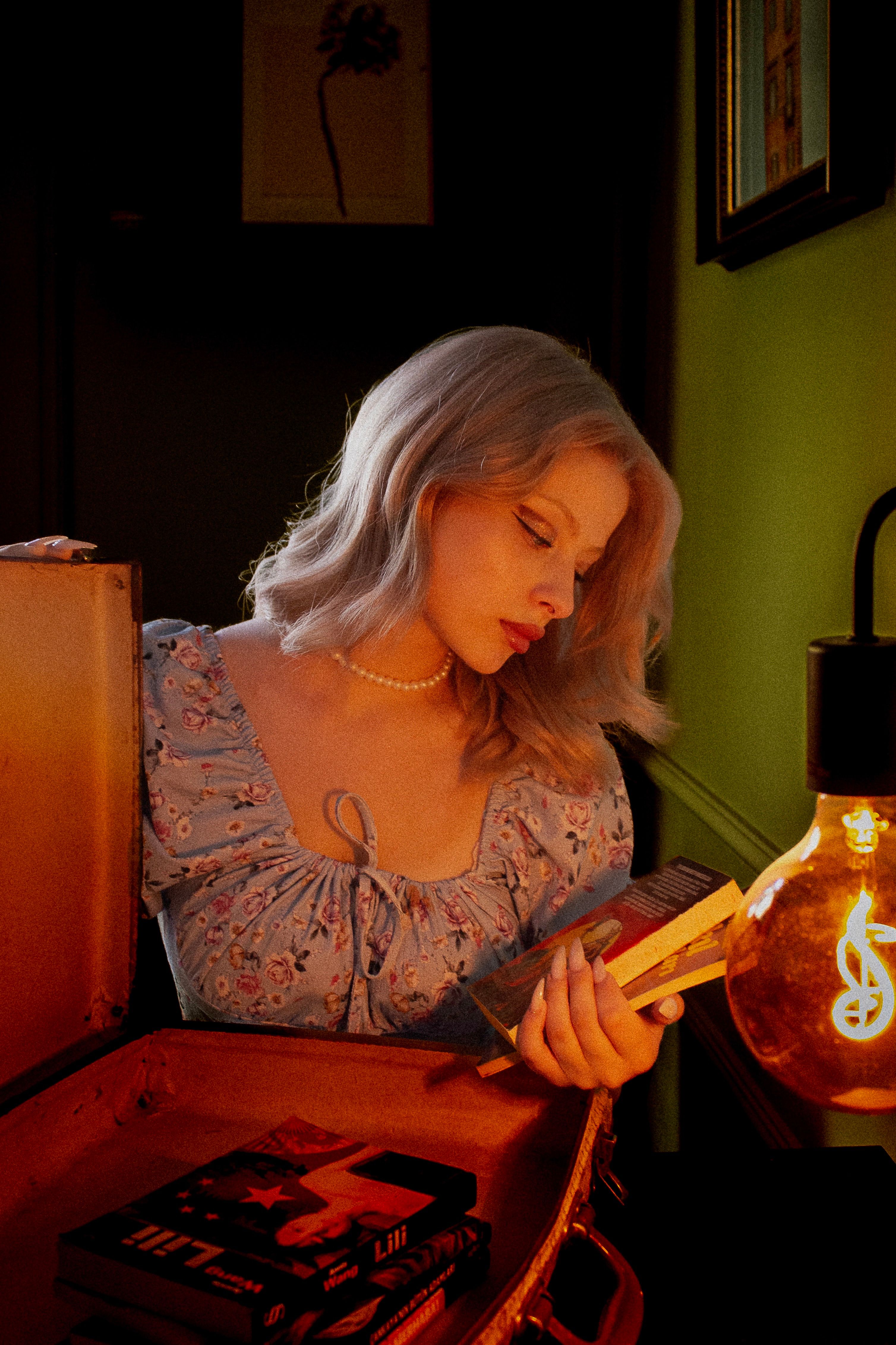 Stylish woman reading a book under warm lighting in a vintage setting.