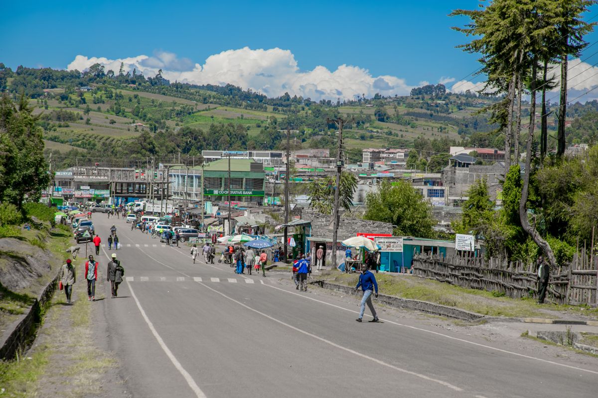 Main street of a small highland town on the climb up from Nakuru, green hills behind the buildings under a clear sky.