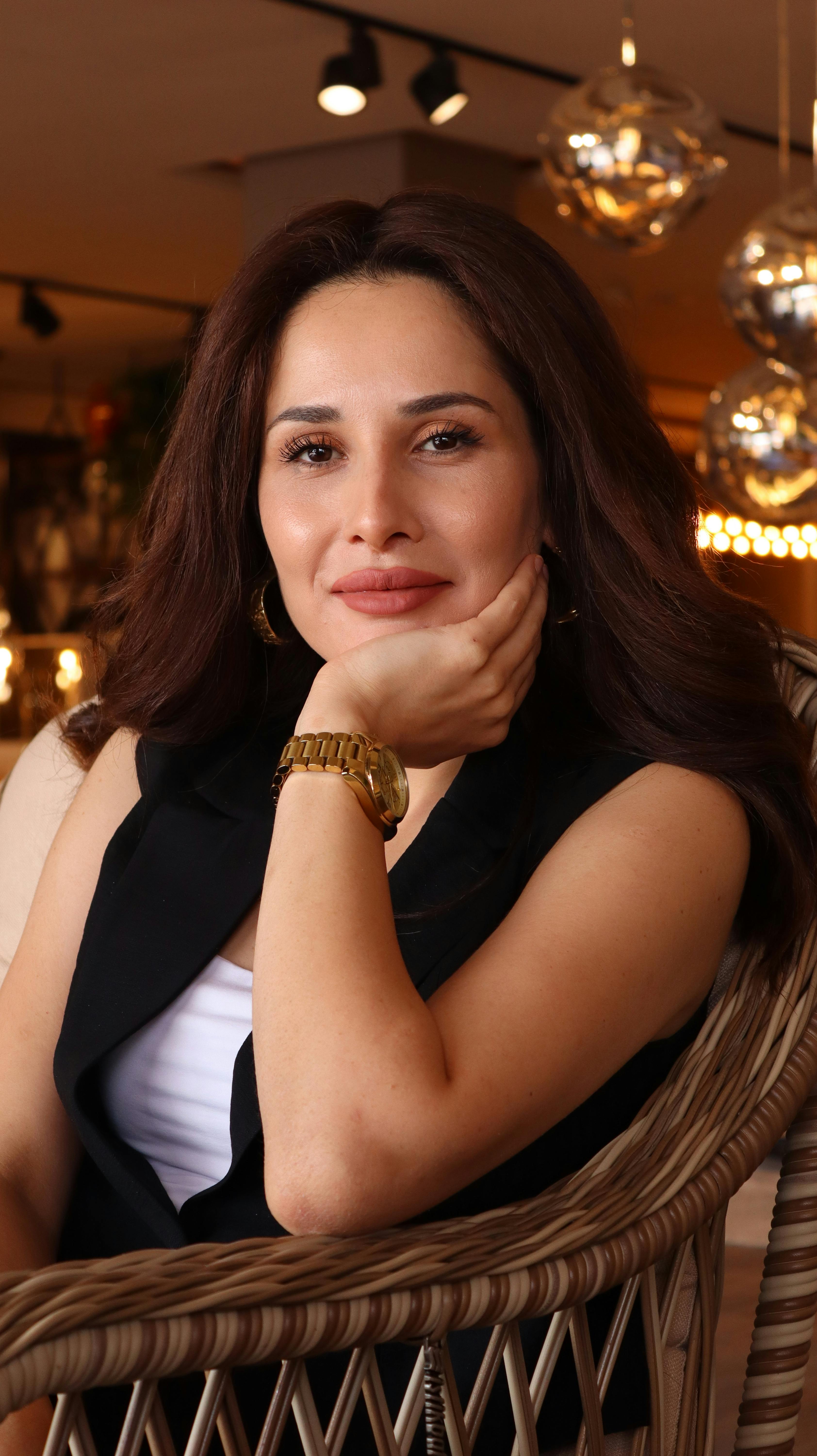 Portrait of a woman smiling while sitting in a rattan armchair indoors, capturing a warm and inviting ambiance.