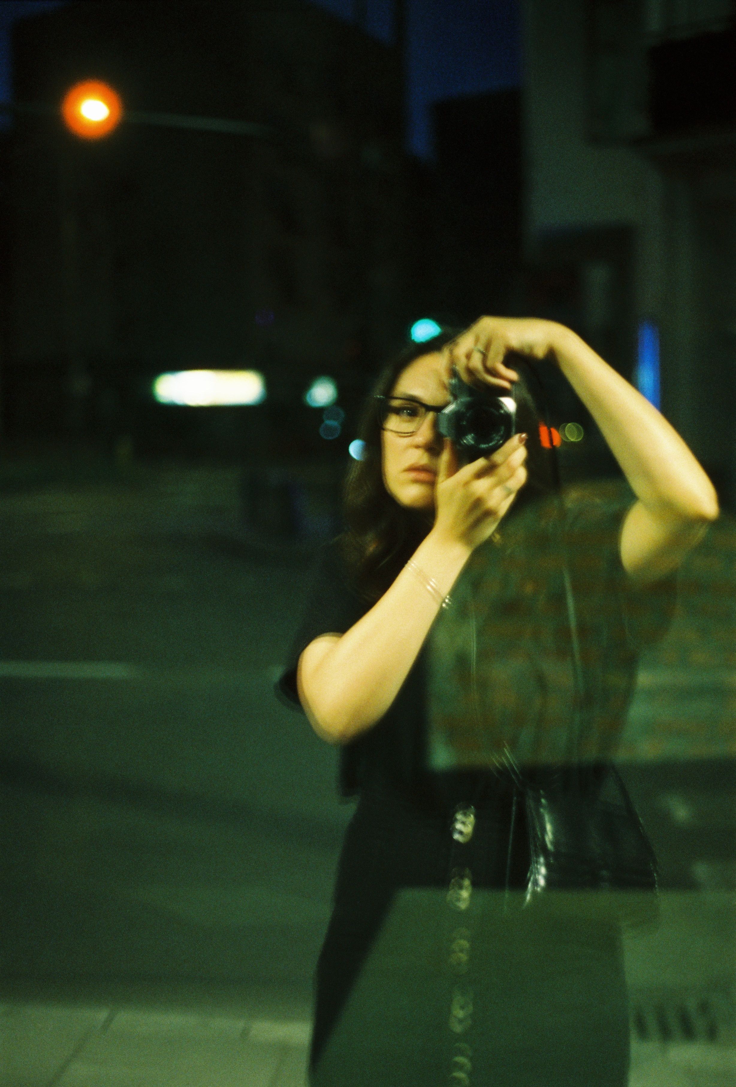 A woman taking a photo through glass at night in urban Warsaw.